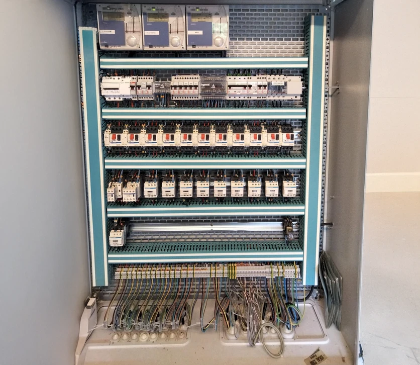 Atelier menuiserie intérieur avec artisan en tee-shirt bleu et casquette utilisant une défonceuse électrique sur panneau bois